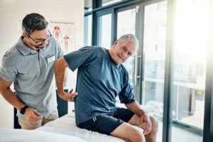 Physical therapist guiding an adult through a stretching exercise beside a treatment table.